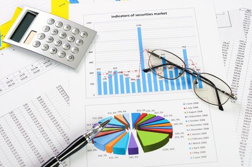 Calculator, eyeglasses, and pen on financial charts with bar and pie graphs.