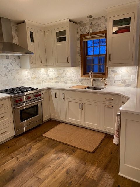 A kitchen with white cabinets , a stove , a sink , and a window.