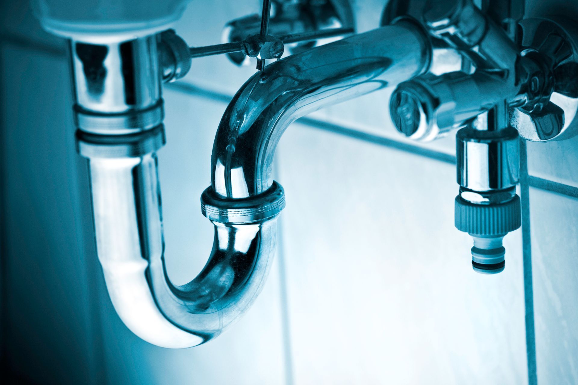 Chrome bathroom sink pipes and drain under a sink in blue lighting