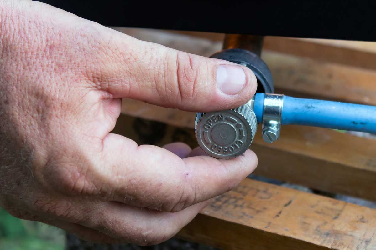 Hand holding a blue hose near a metal connector on a wooden surface