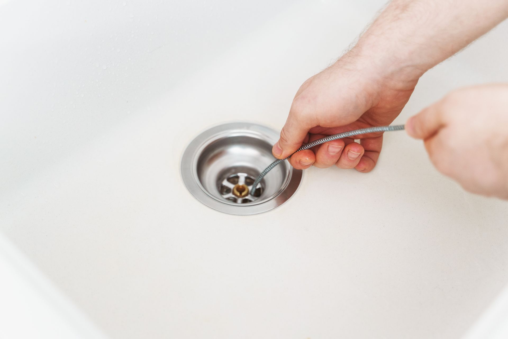 Hands using tweezers to remove debris from a bathroom sink drain