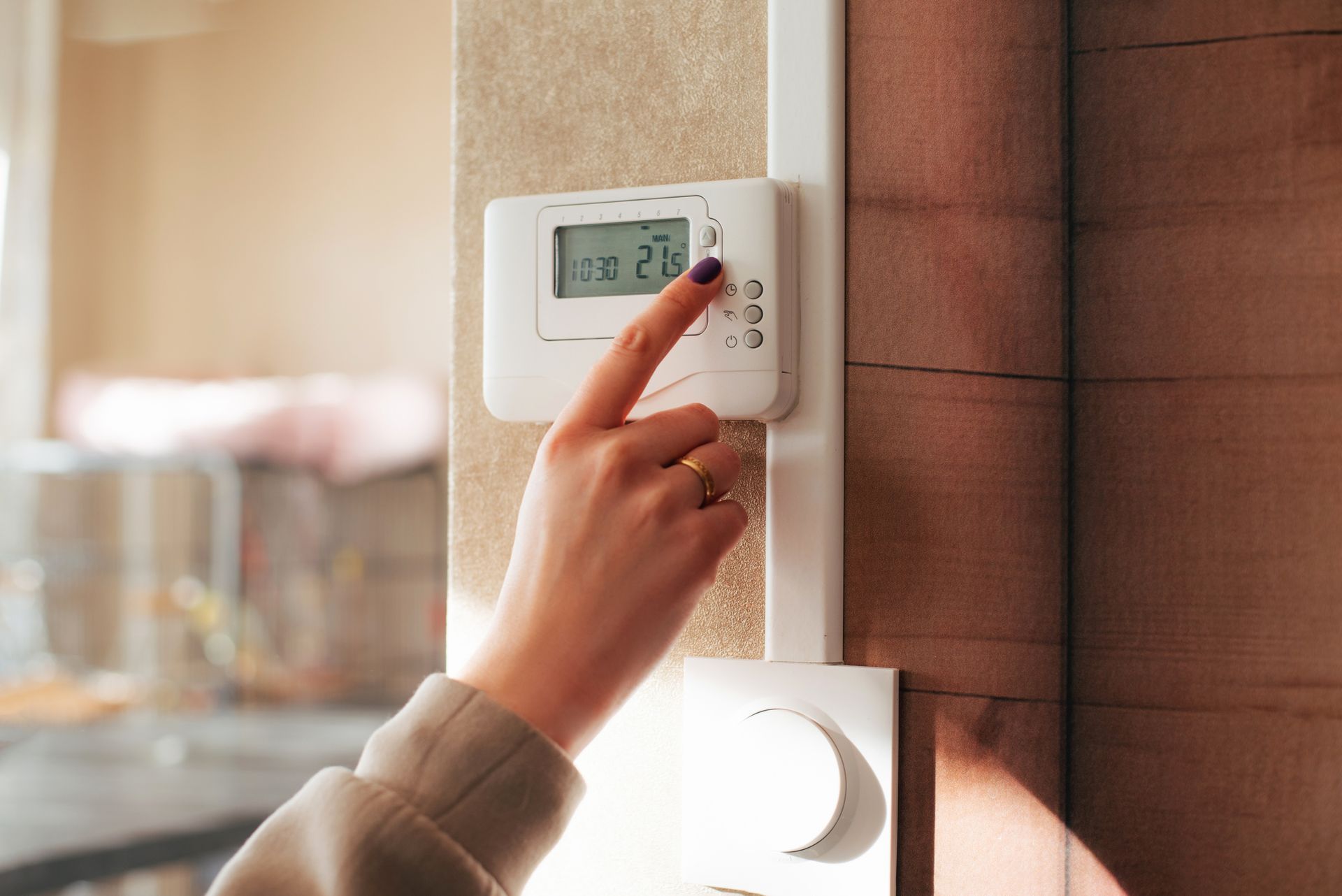 Hand adjusting a white wall thermostat with a digital display in a warmly lit room