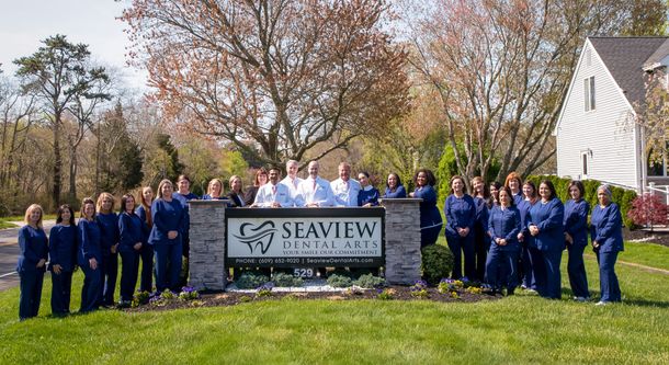 Seaview Dental Care staff posing outdoors by sign. People in blue scrubs, sunny day.