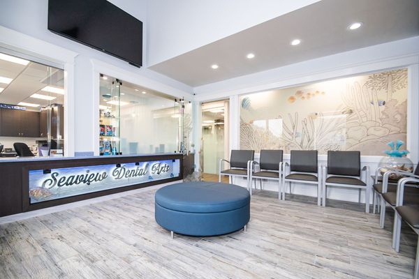 Dental office waiting room with blue ottoman, gray chairs, and decorative wall art.