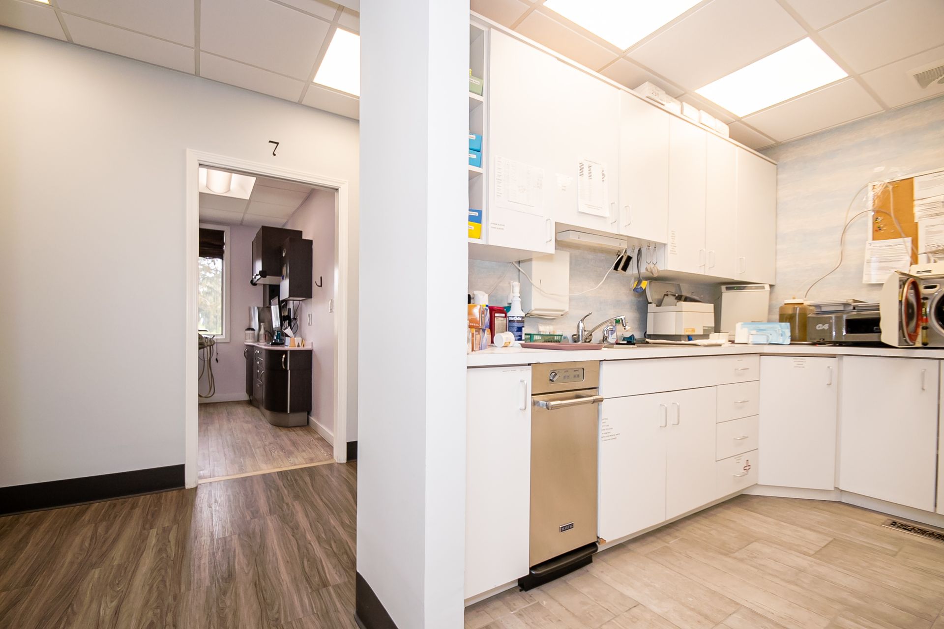 A white office kitchen with appliances and a doorway leading to another room.