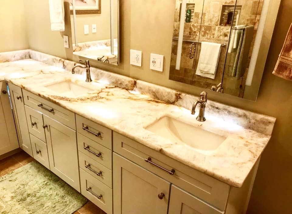 A bathroom vanity with two sinks, marble countertop, and white cabinets. Mirrors, faucets, and a towel rack are visible.