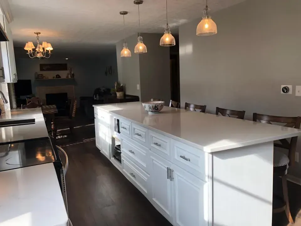 Bright kitchen with white cabinets, long island, pendant lights, and view into living area.