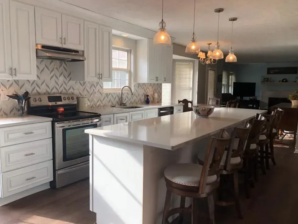 White kitchen with a large island, stainless steel appliances, and pendant lights.