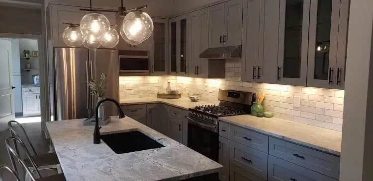 Modern kitchen with white cabinets, stainless steel appliances, and a marble countertop island.