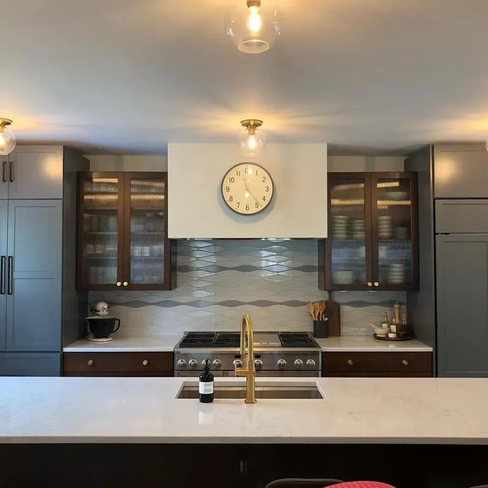 Modern kitchen with island, range, and cabinets in gray, brown, and white. Gold fixtures and a large clock.