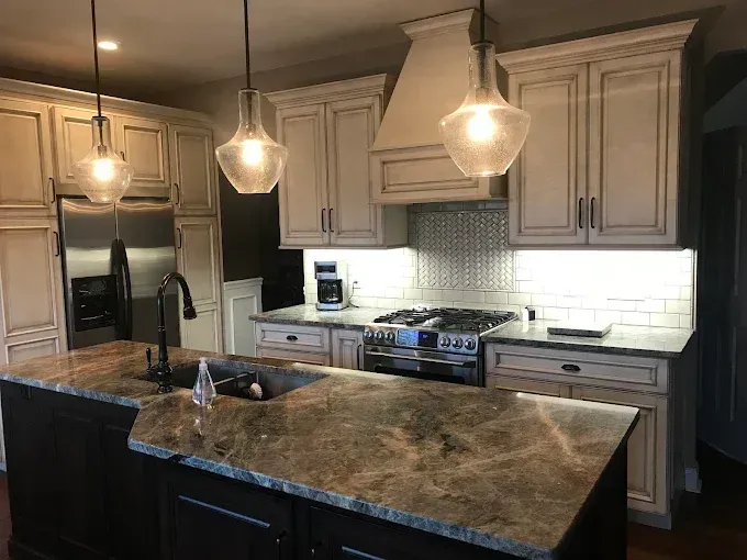 Kitchen with cream cabinets, dark island, granite countertops, stainless steel appliances, and pendant lights.