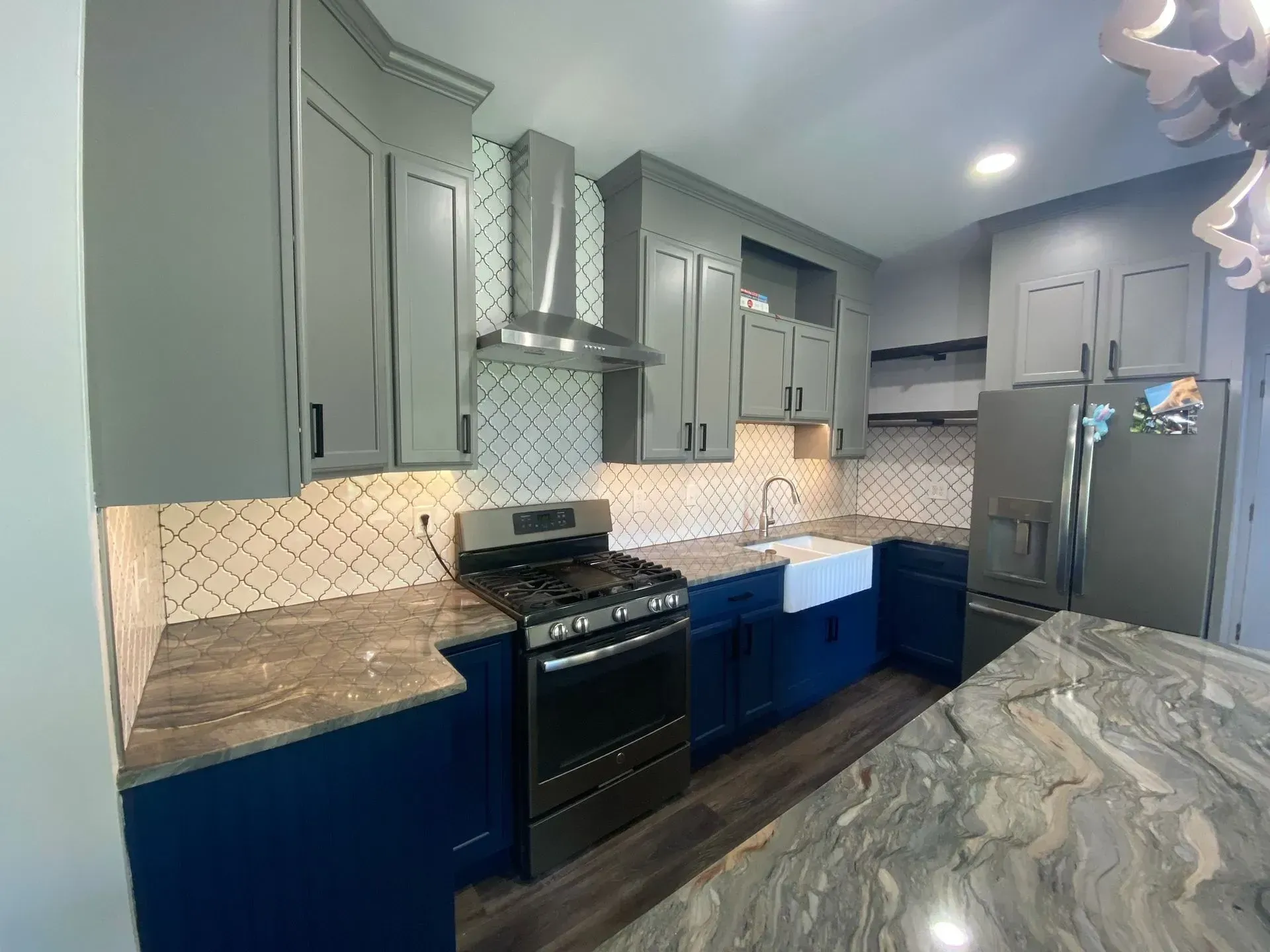 A modern kitchen with blue and gray cabinets, stainless steel appliances, and a marble countertop.