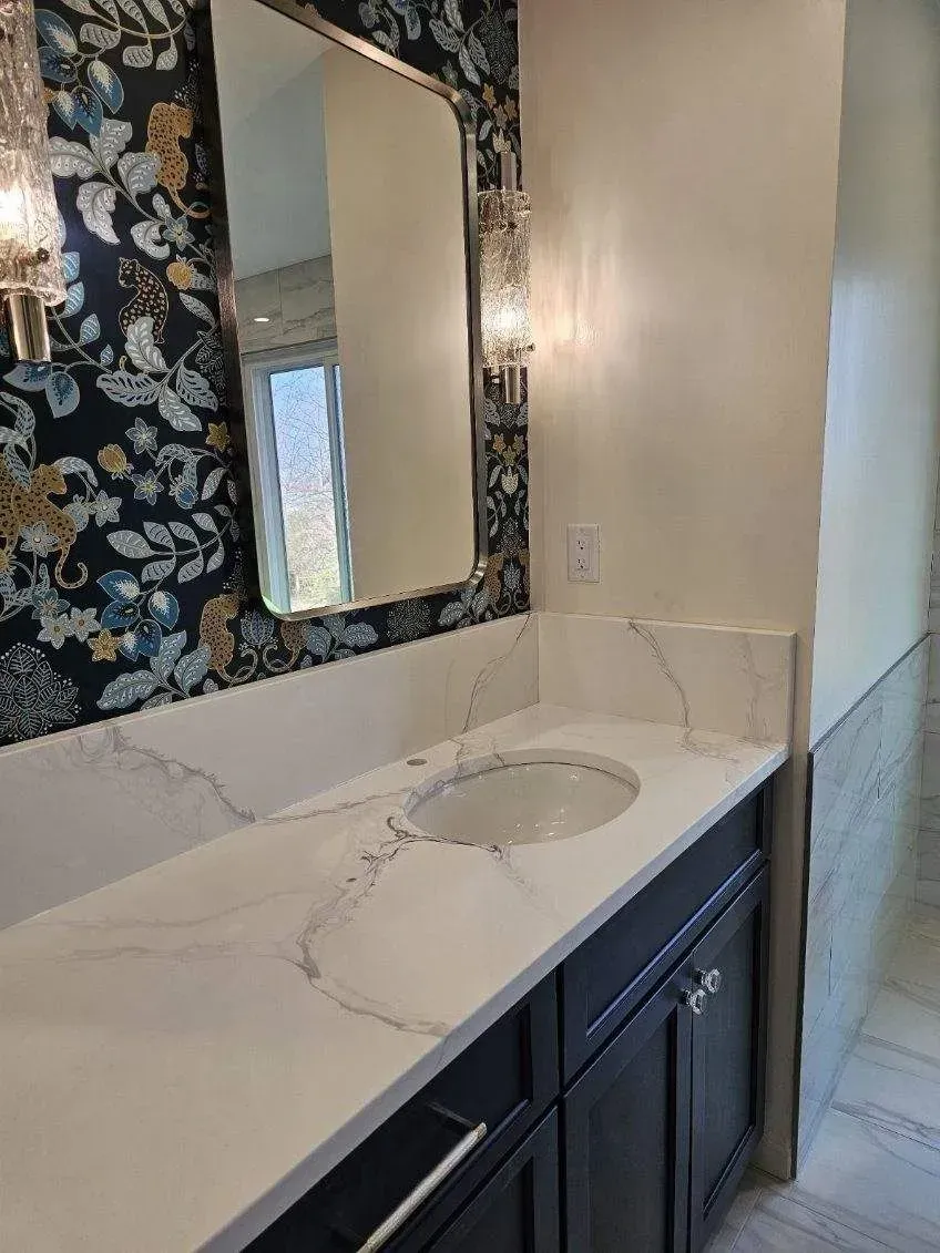 Bathroom vanity with dark cabinets, white countertop, floral wallpaper, and mirror.