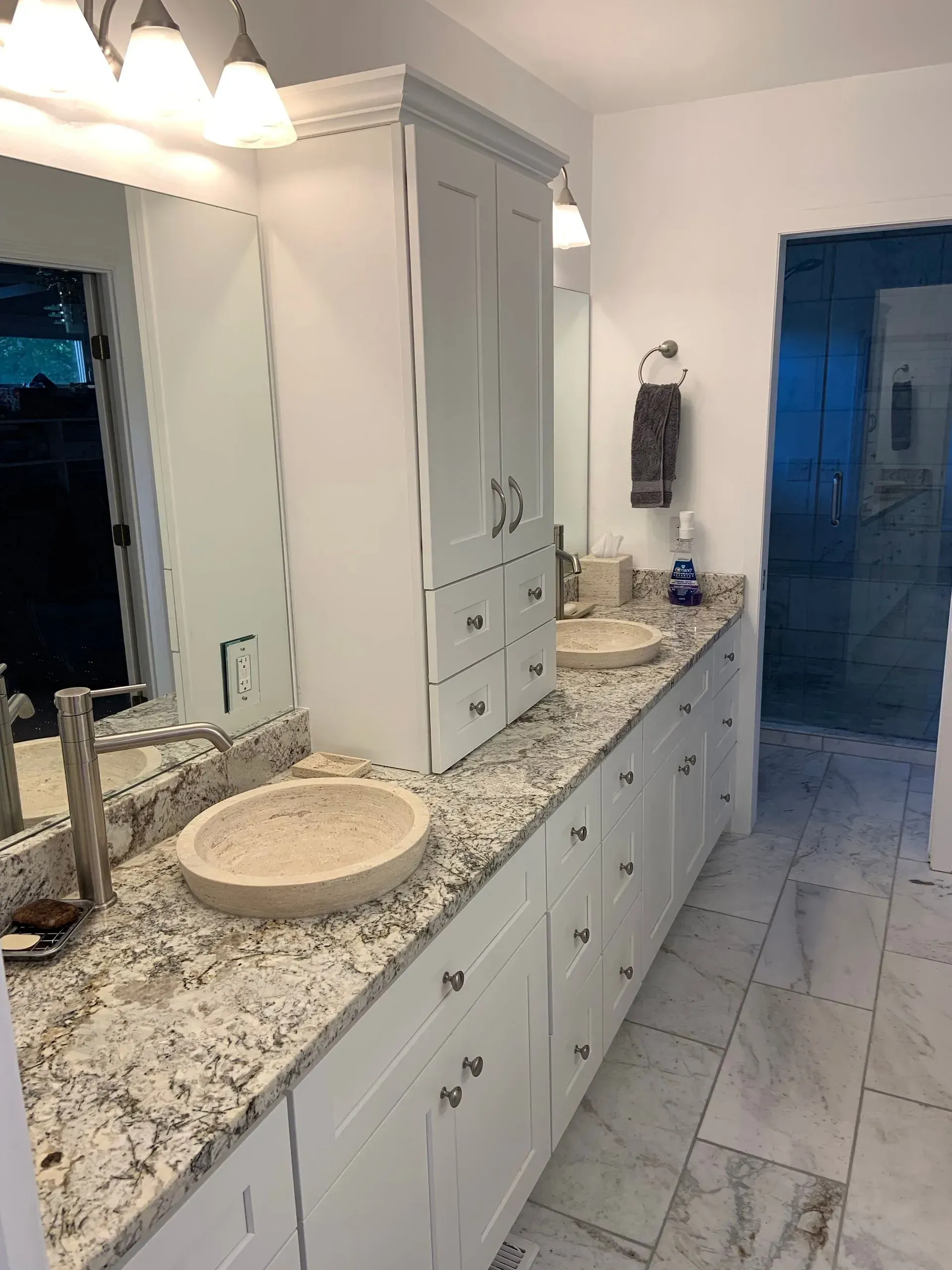 Bathroom with white cabinetry, granite countertop, two sinks, and a glass shower.