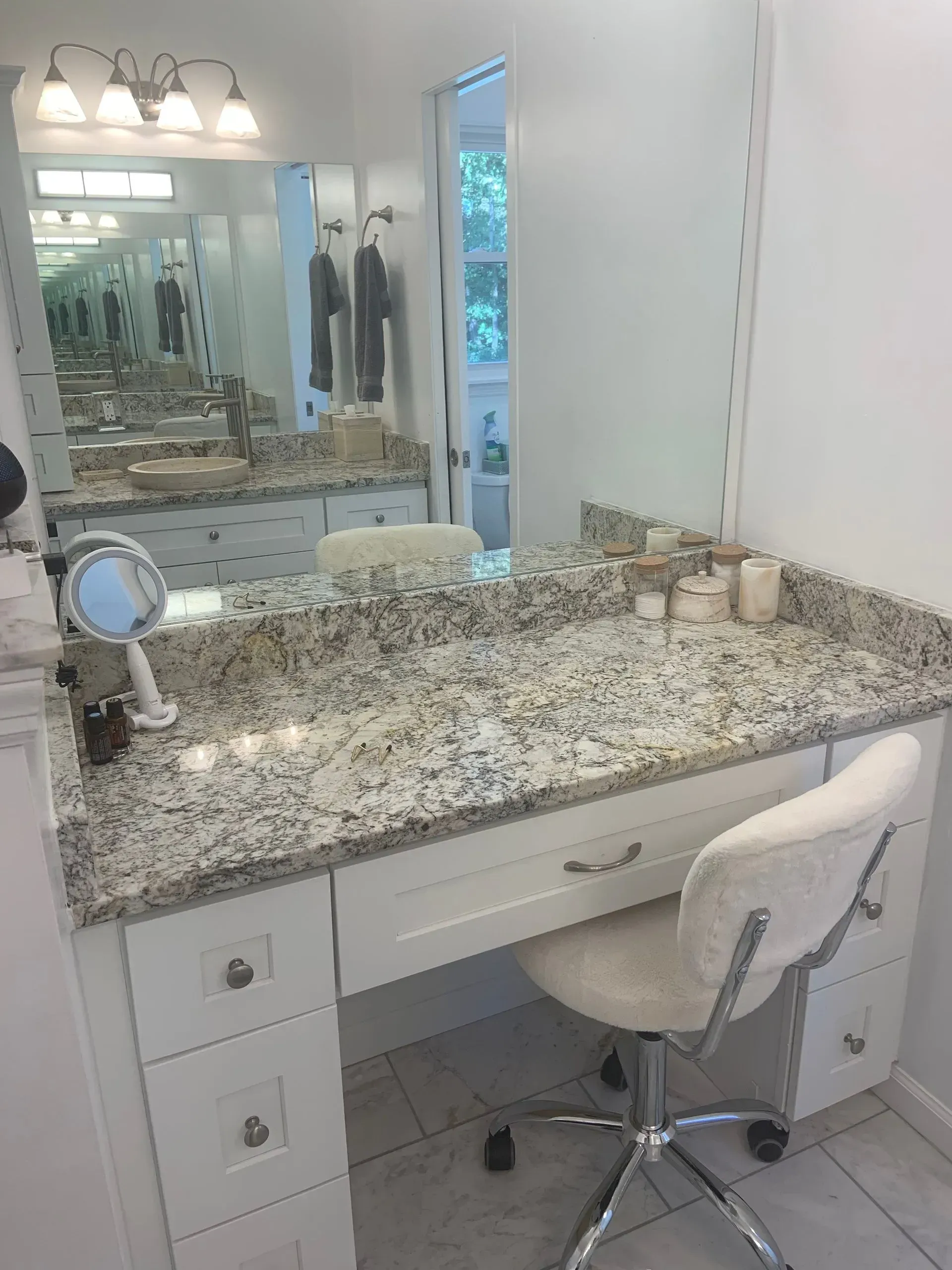 Vanity with granite countertop, white cabinets, mirror, and a fluffy white chair.