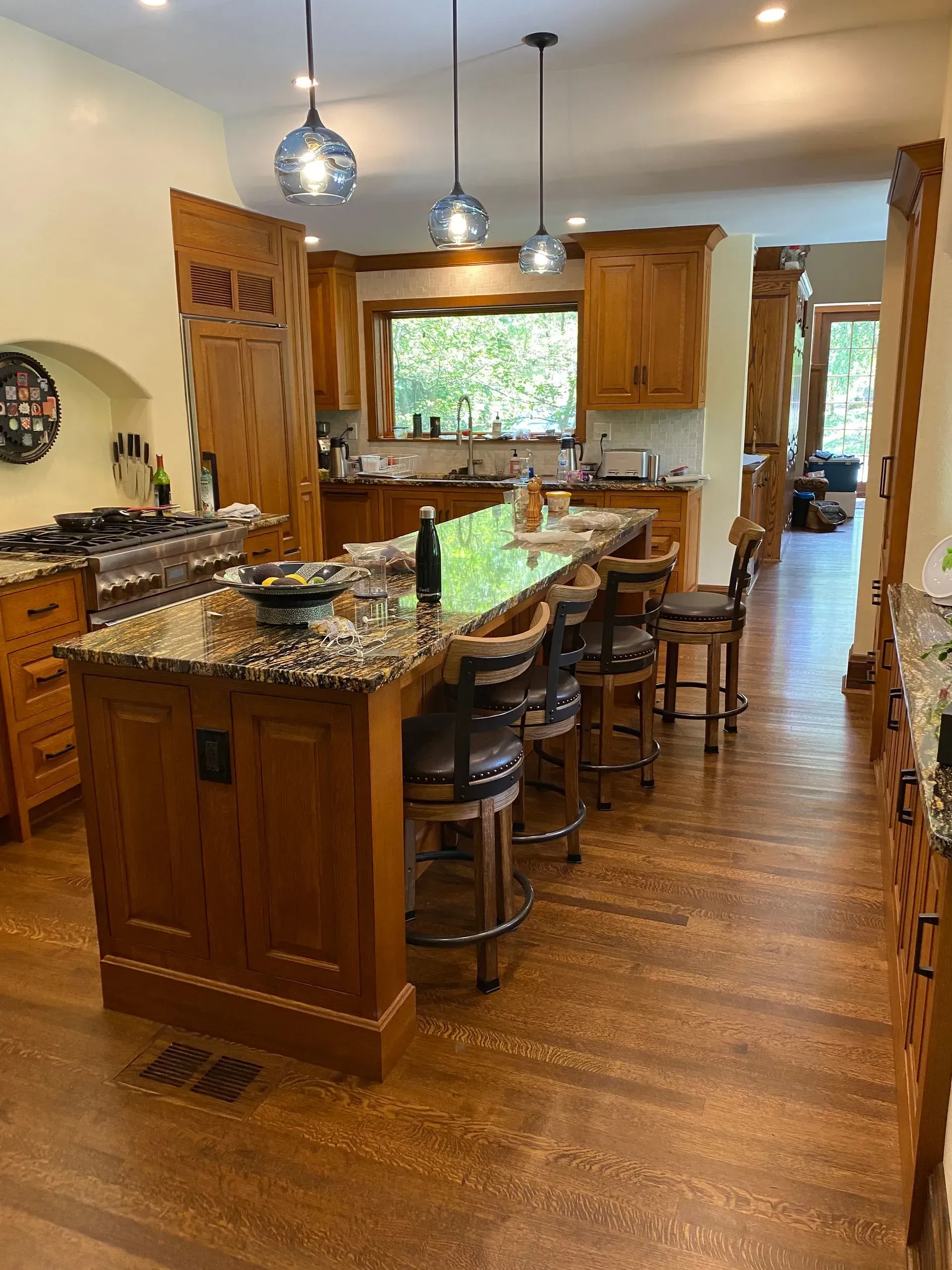 Spacious kitchen with a large island, wood cabinets, and hardwood floors. Three hanging lights illuminate the island.