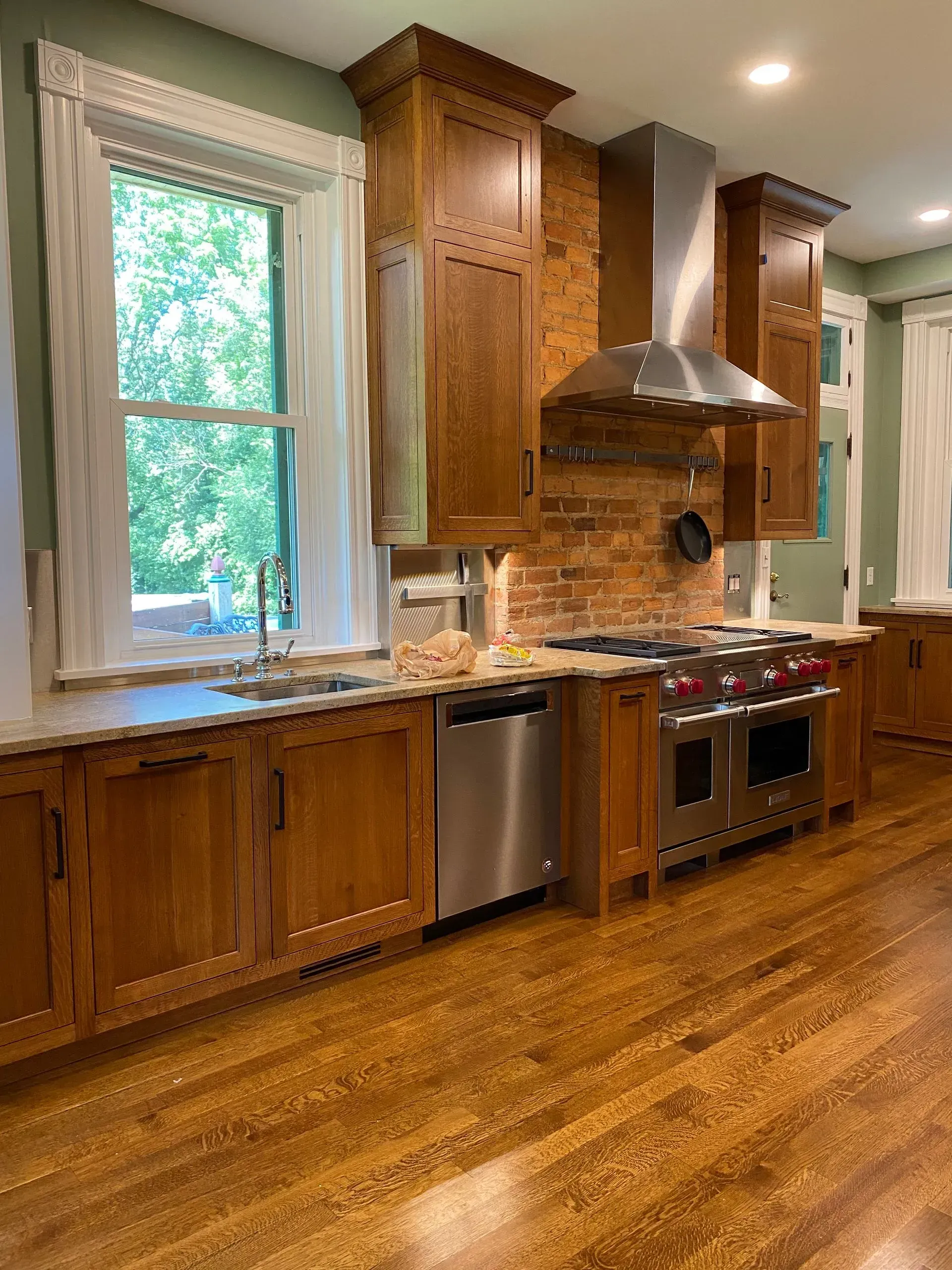 Wooden kitchen with stainless steel appliances, exposed brick backsplash, and a window.