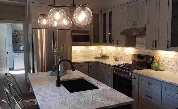 Modern kitchen with island, stainless steel appliances, gray cabinets, and bubble pendant lights.