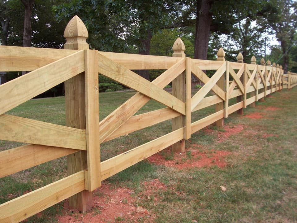 Wooden split-rail fence with X-braced panels along a grassy path by trees