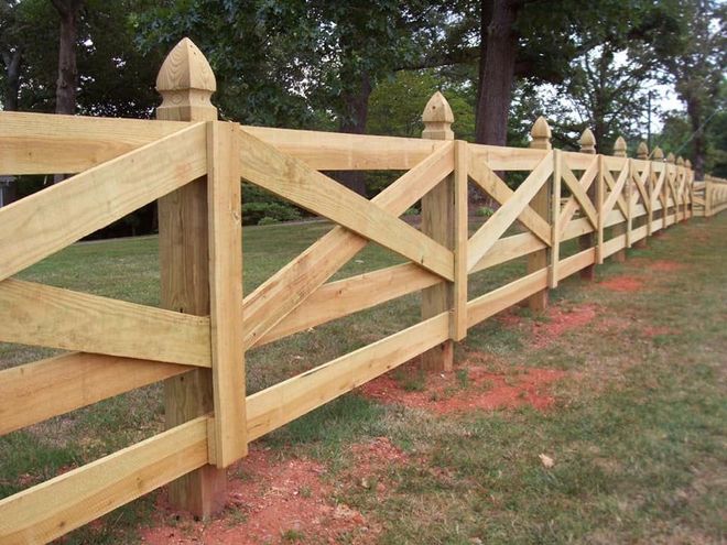 Wooden split-rail fence with X-braced panels along a grassy path by trees