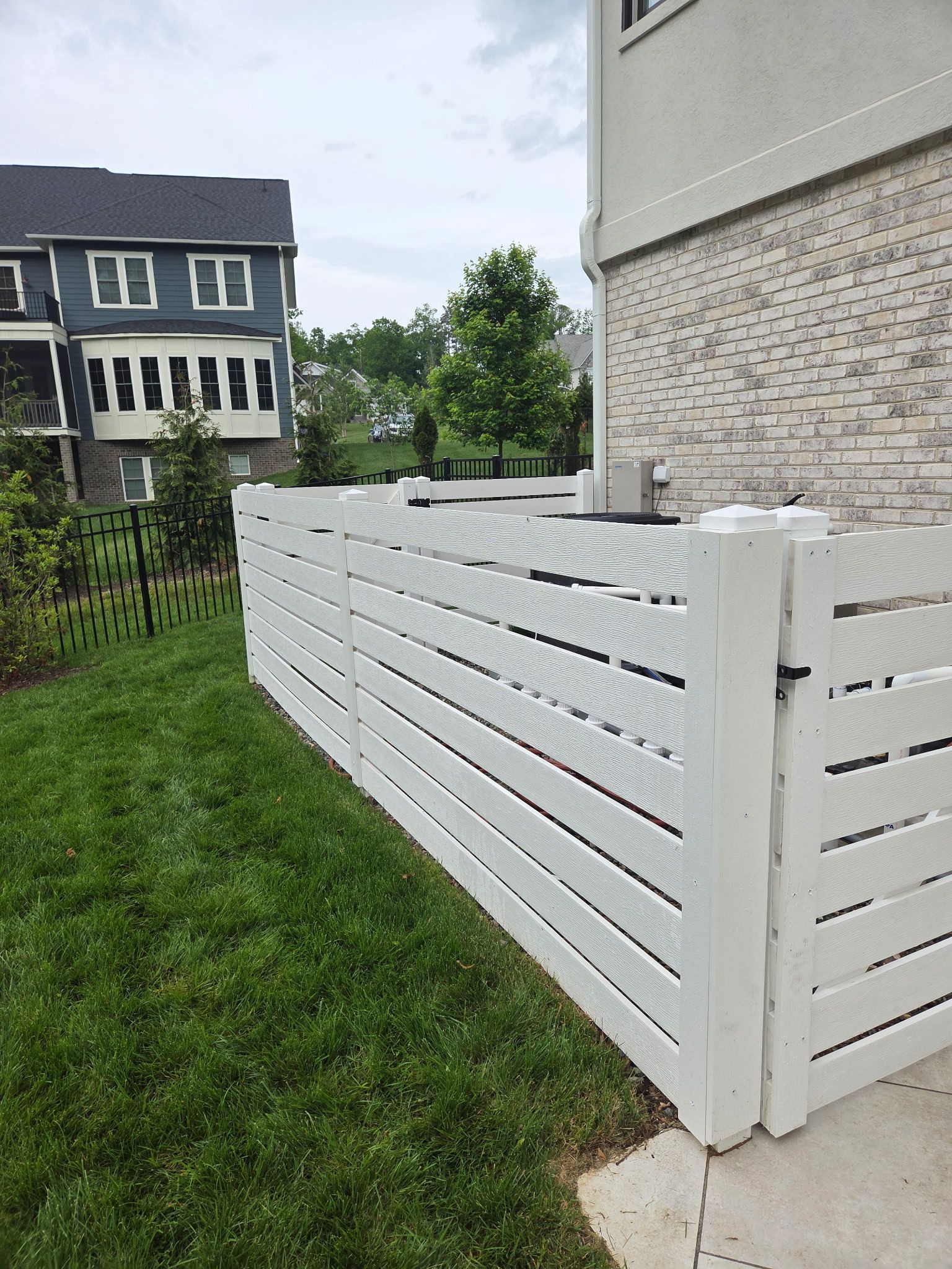White slatted fence along a grassy side yard beside a house and neighboring homes
