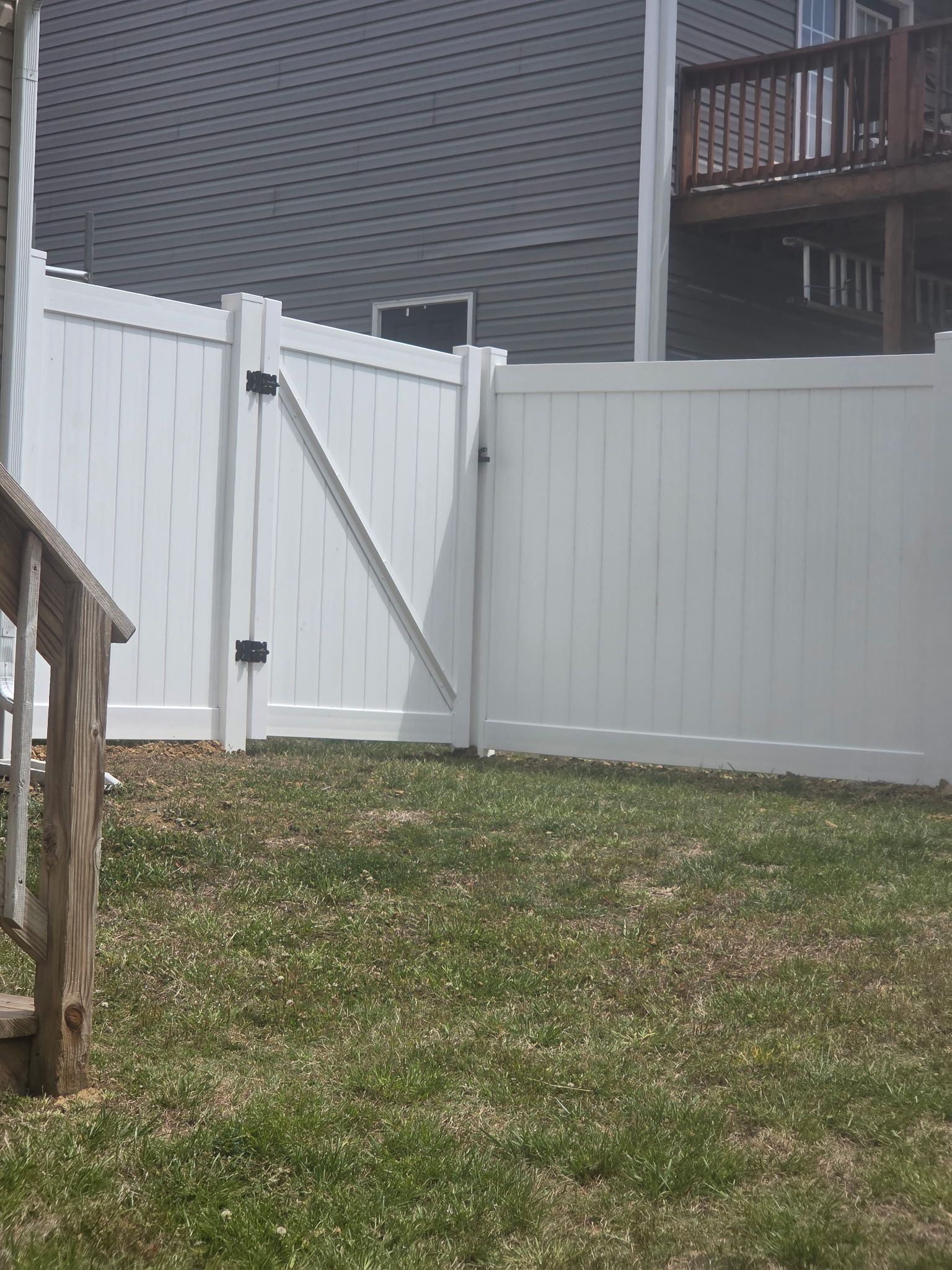White vinyl backyard fence with a swinging gate beside a house and grassy yard