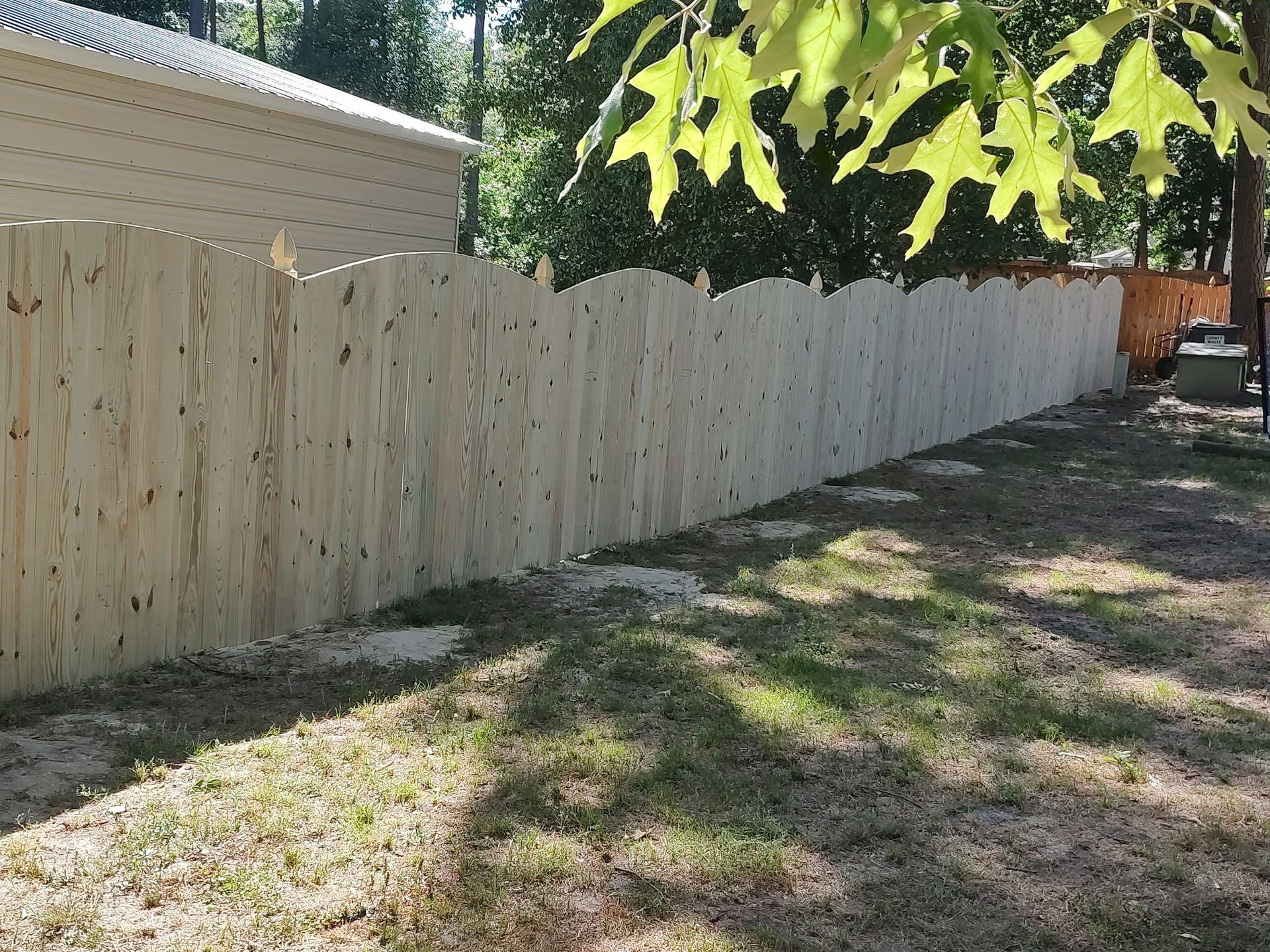 Wooden privacy fence along a shaded backyard path beside a beige house, with trees overhead.