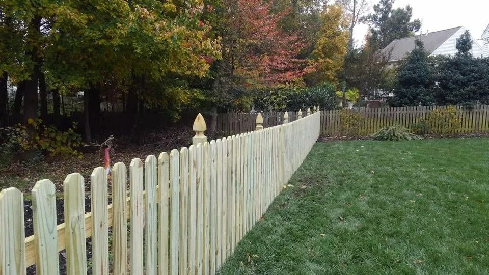 White picket fence beside a green lawn with autumn trees in the background