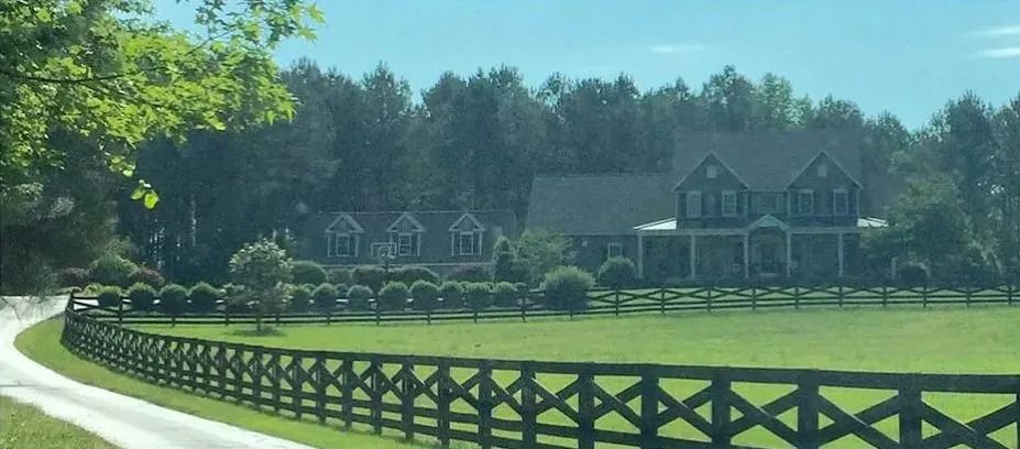 Sunny rural house behind black fence and green field under blue sky