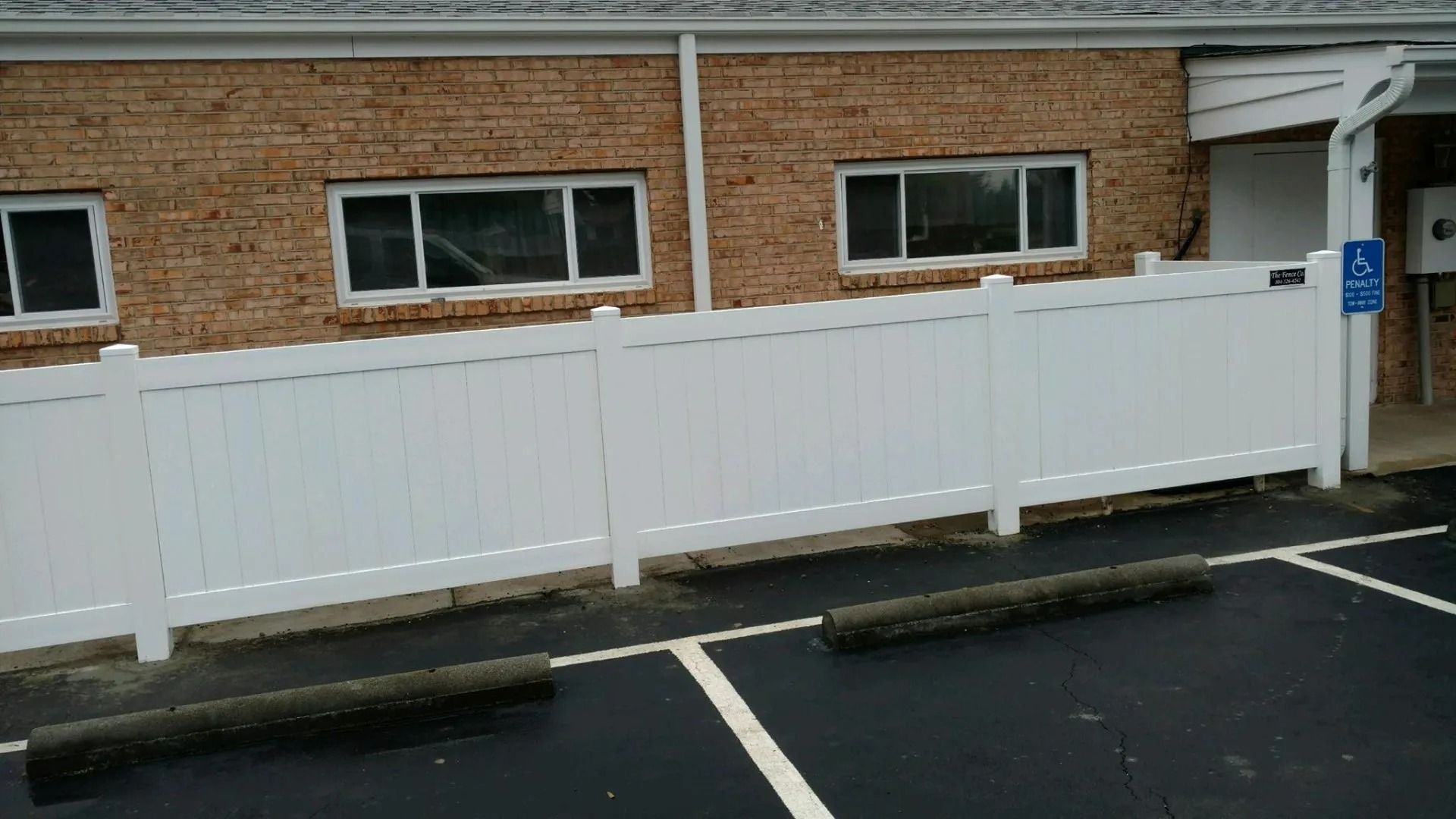 White fence in front of a brick building with parking spaces and a small ramp entrance