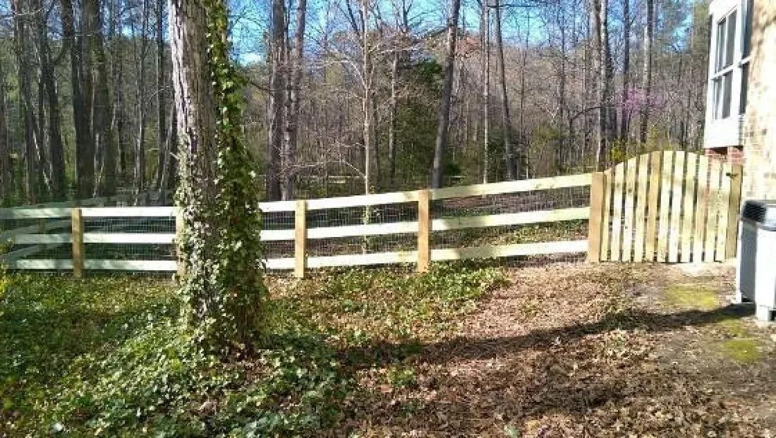 Wooded backyard with a white wooden fence and a house at the right edge