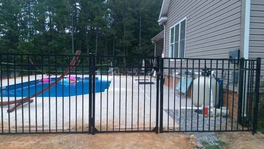 Backyard pool with a black metal fence, white tarp-covered area, and a house beside it