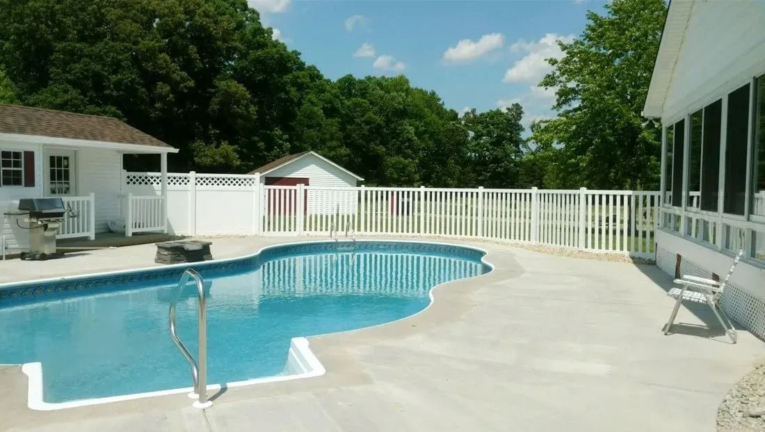 Backyard pool with blue water, white fence, and patio beside a house under a sunny sky