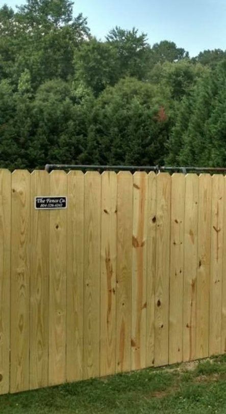 Wooden privacy fence with a black sign, backed by dense green trees under a clear sky