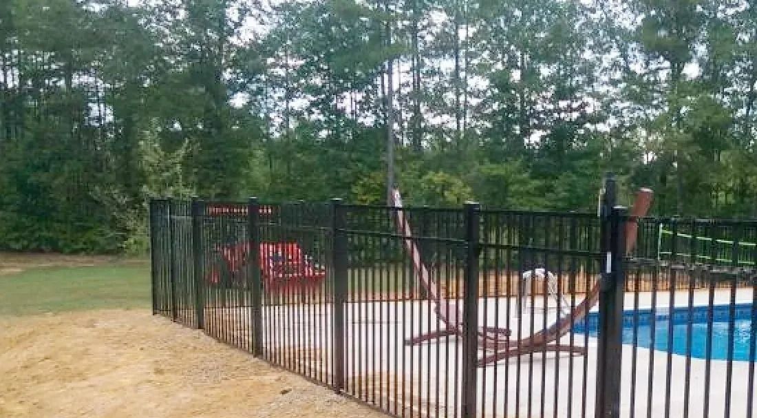 Backyard fenced pool area with black metal fence, red slide, and trees in the background