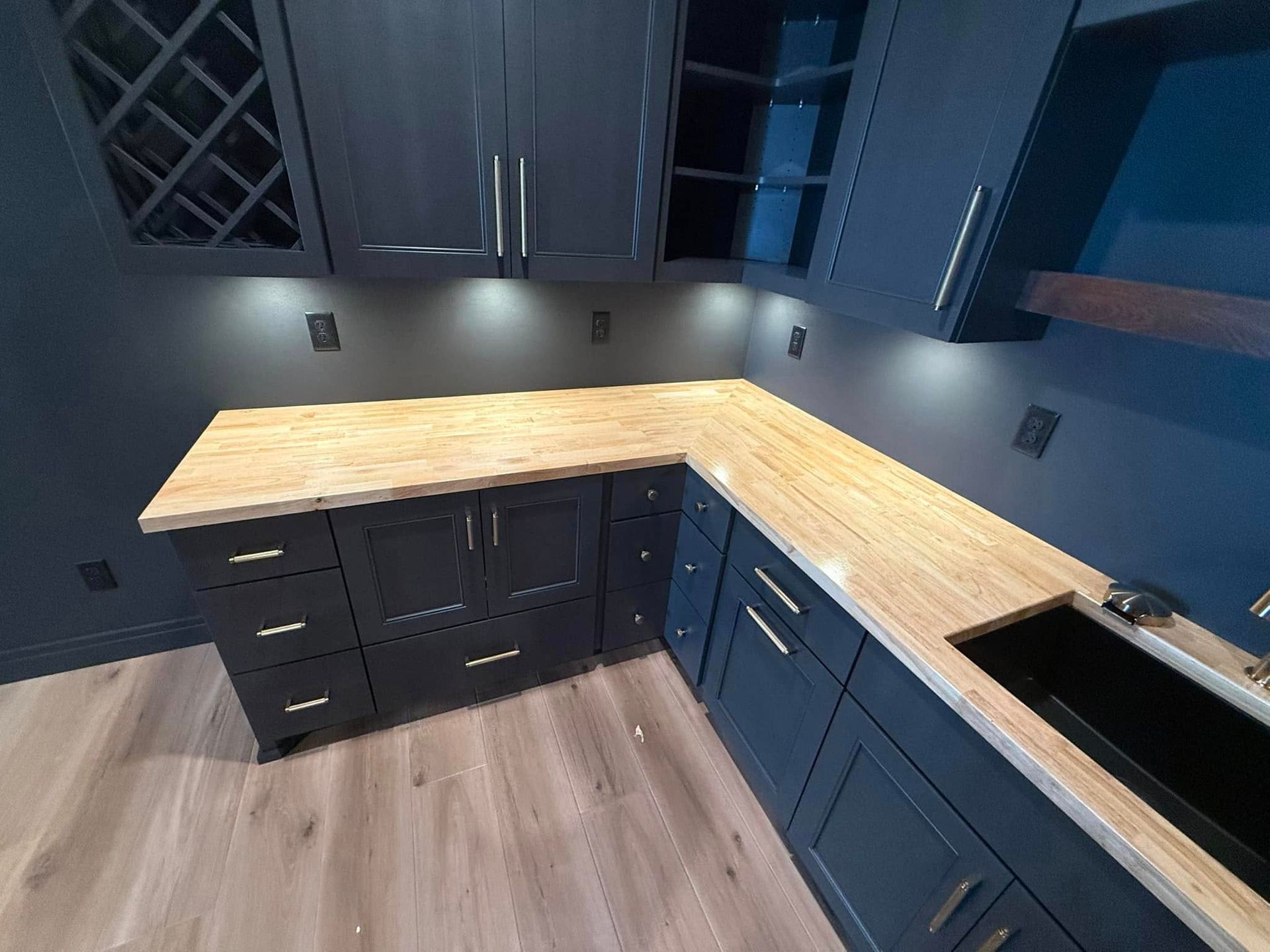 Dark blue bar with wood countertop, wine rack, cabinets, and a sink.