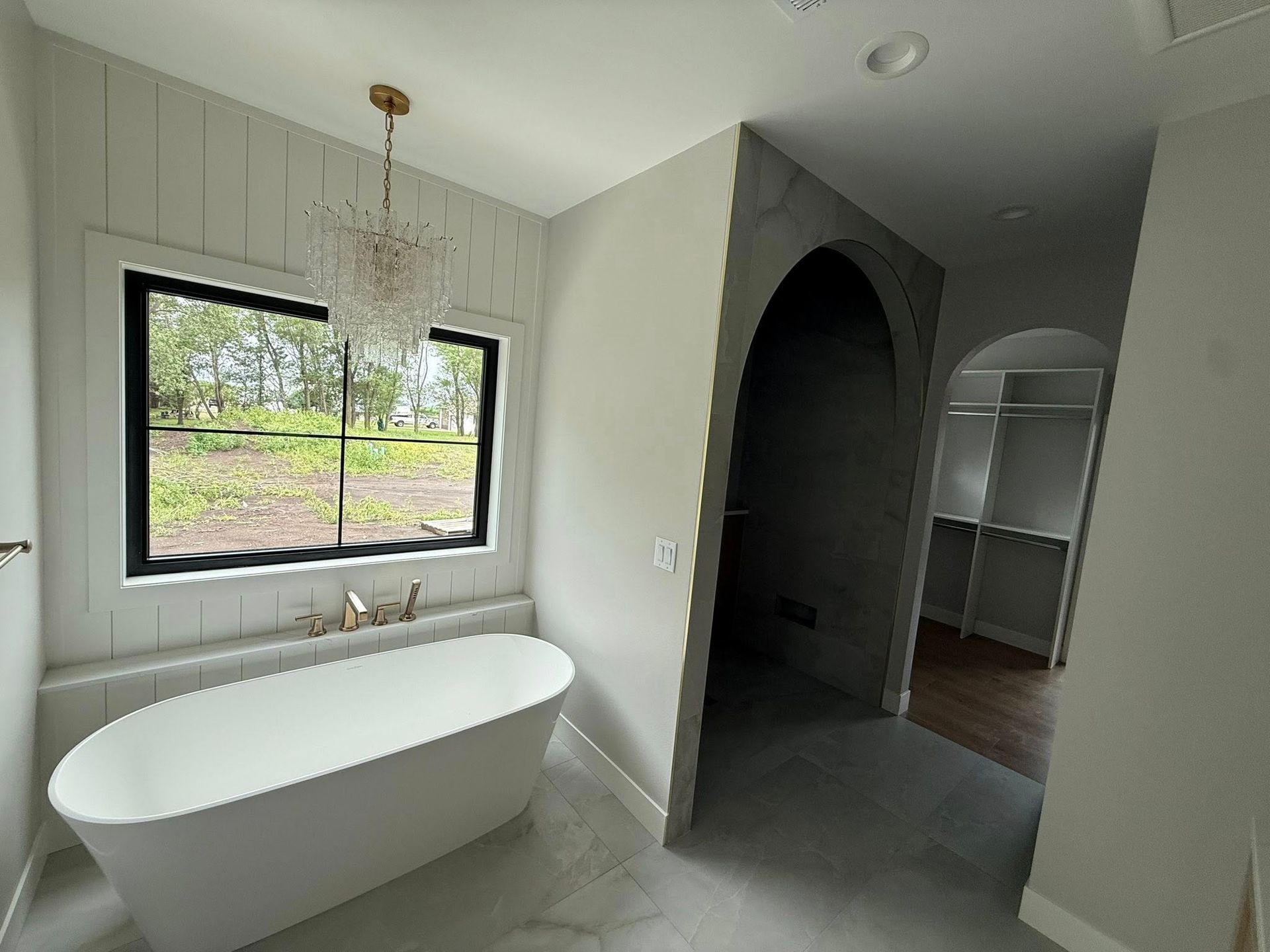 Bathroom with white tub, black-framed window, gray walls, and an arched doorway leading to a closet.