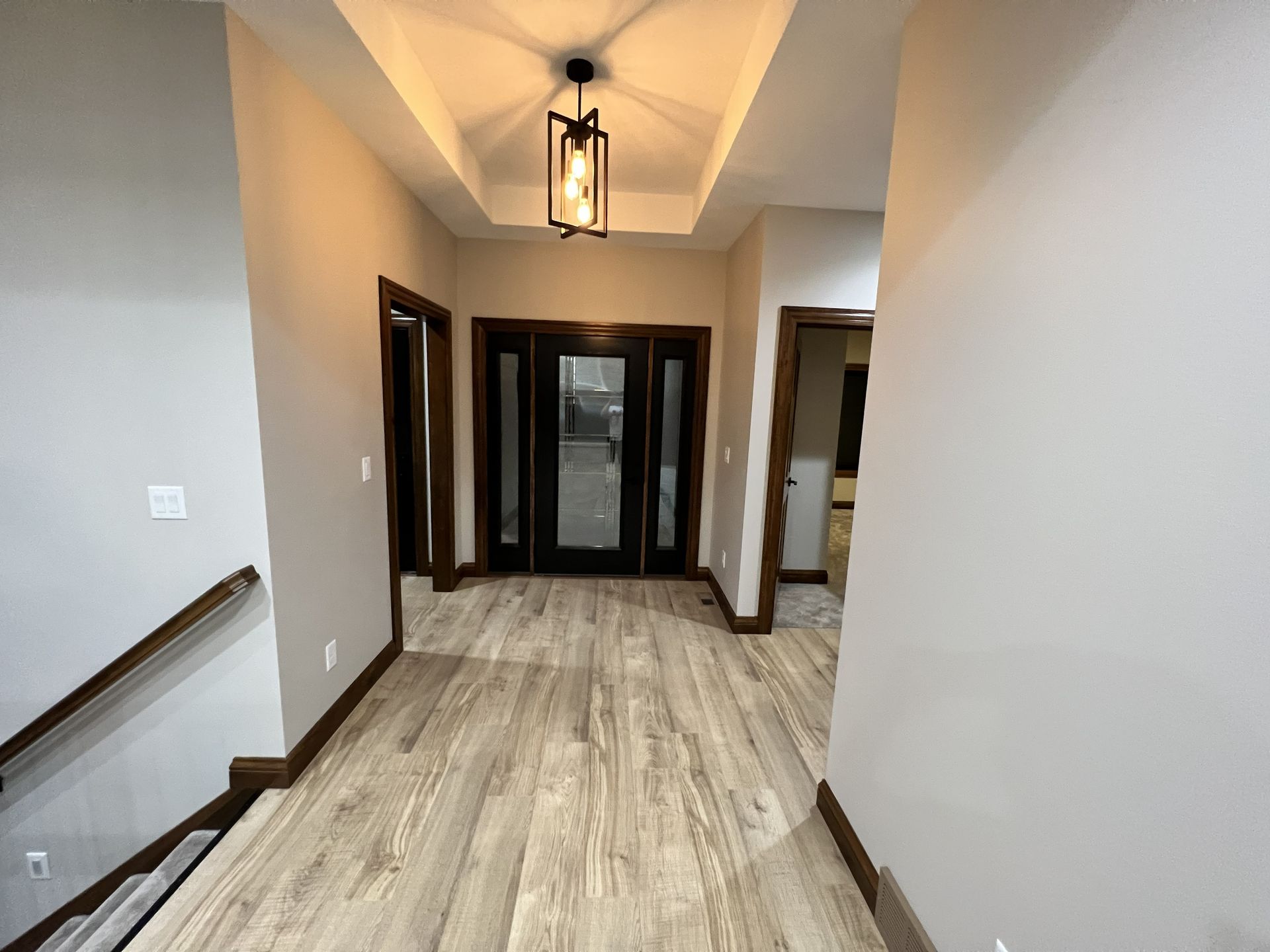 Hallway with light wood floors and dark wood trim. Black front door and geometric light fixture.