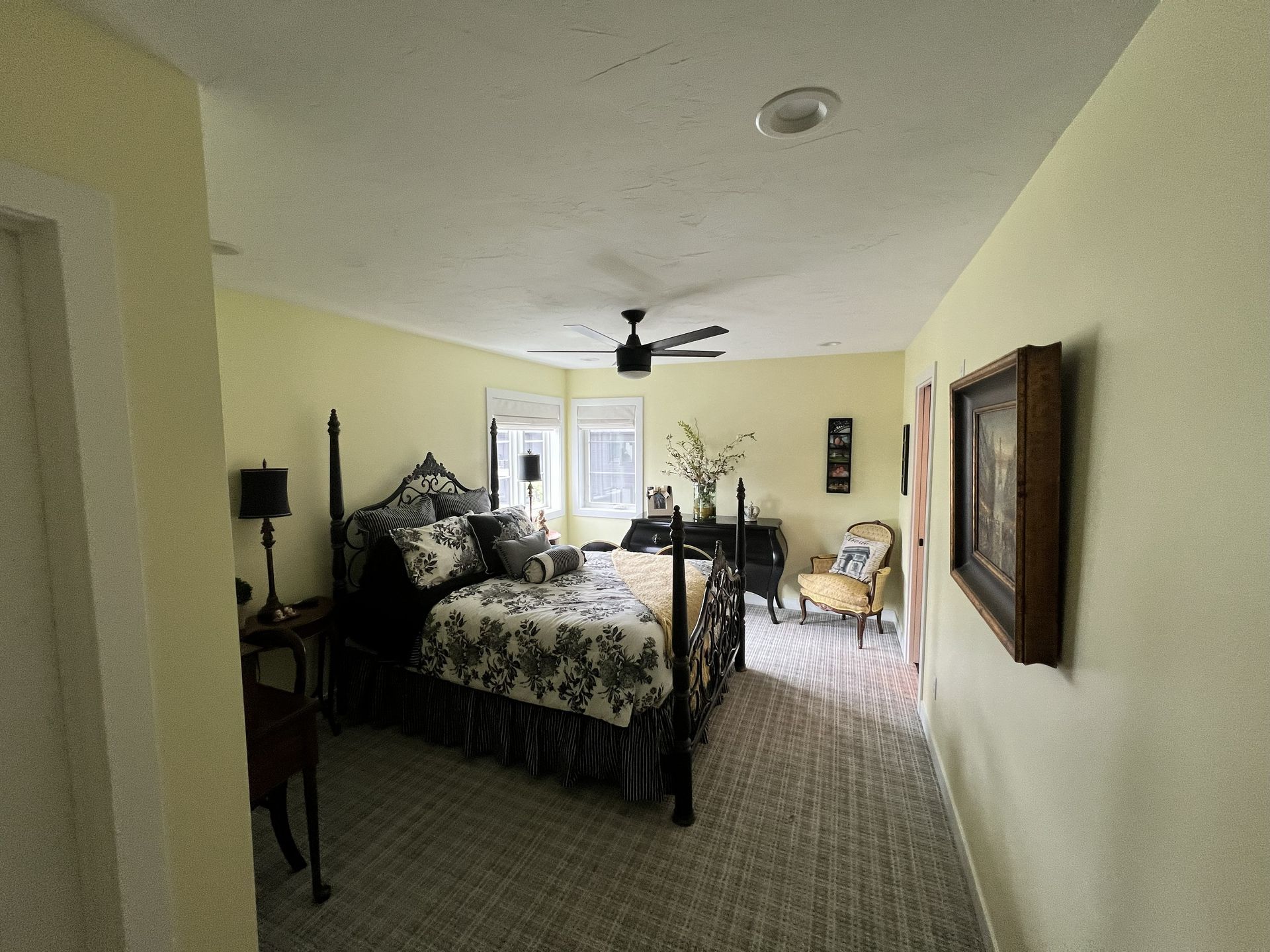 Bedroom with four-poster bed, floral bedding, black furniture, and yellow walls.