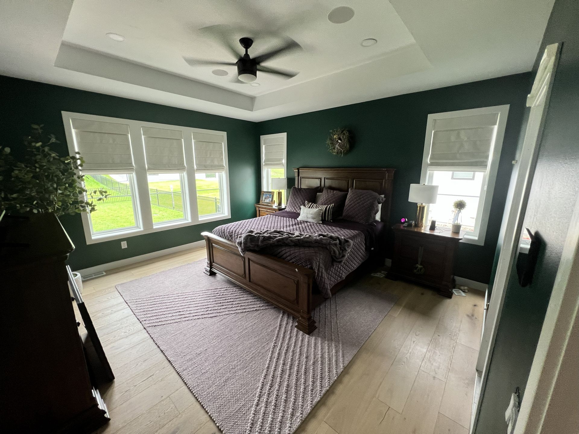Bedroom with dark green walls, a wooden bed, and light-colored wood flooring; a rug is under the bed.