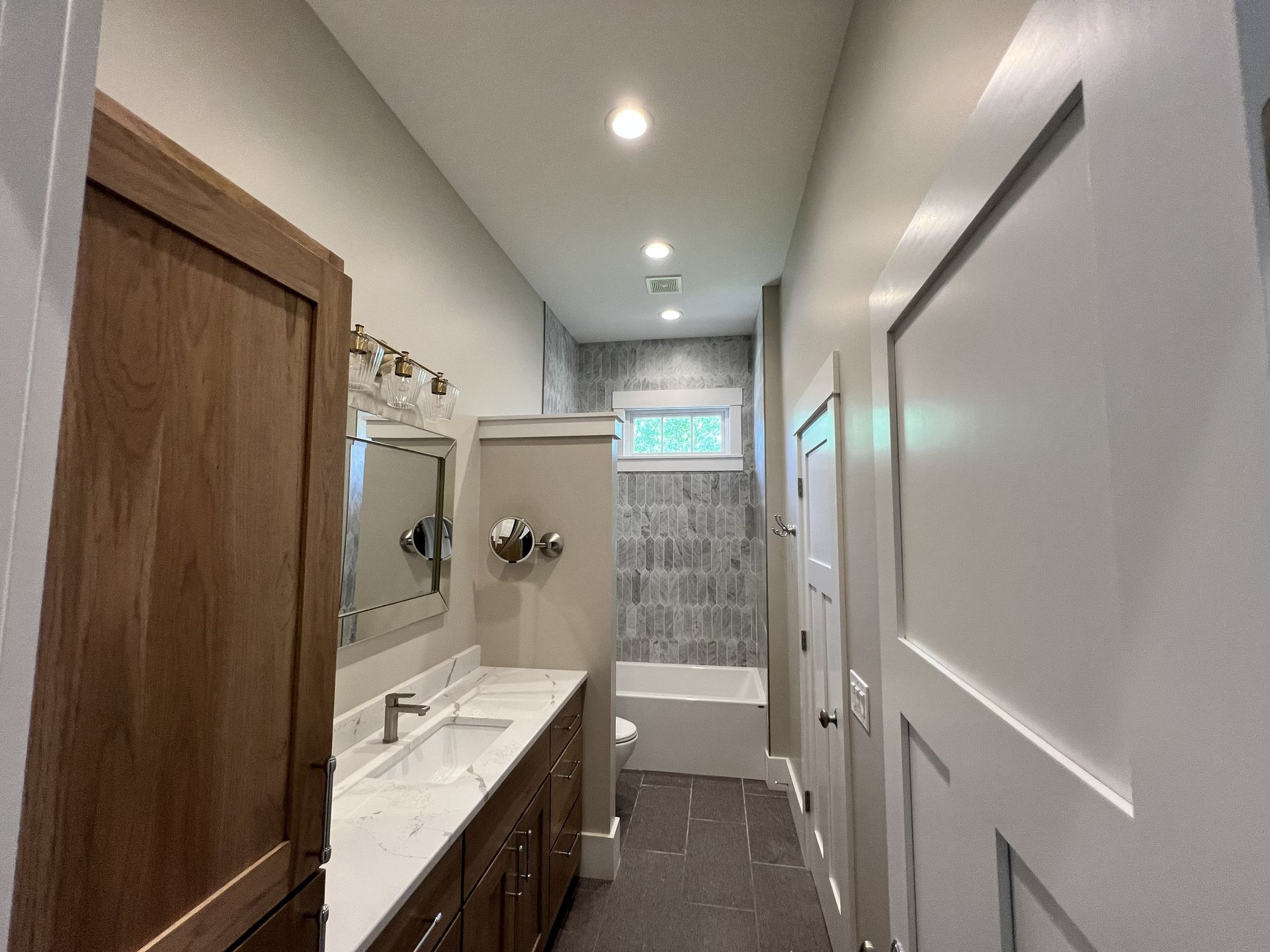 Bathroom with wooden vanity, long counter, and tiled shower area.