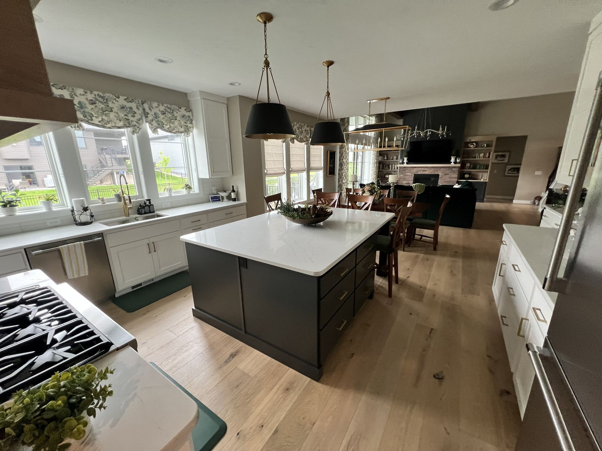 Spacious kitchen with a large island, countertops, and wood floors. Dining area in the background with windows and a fireplace.