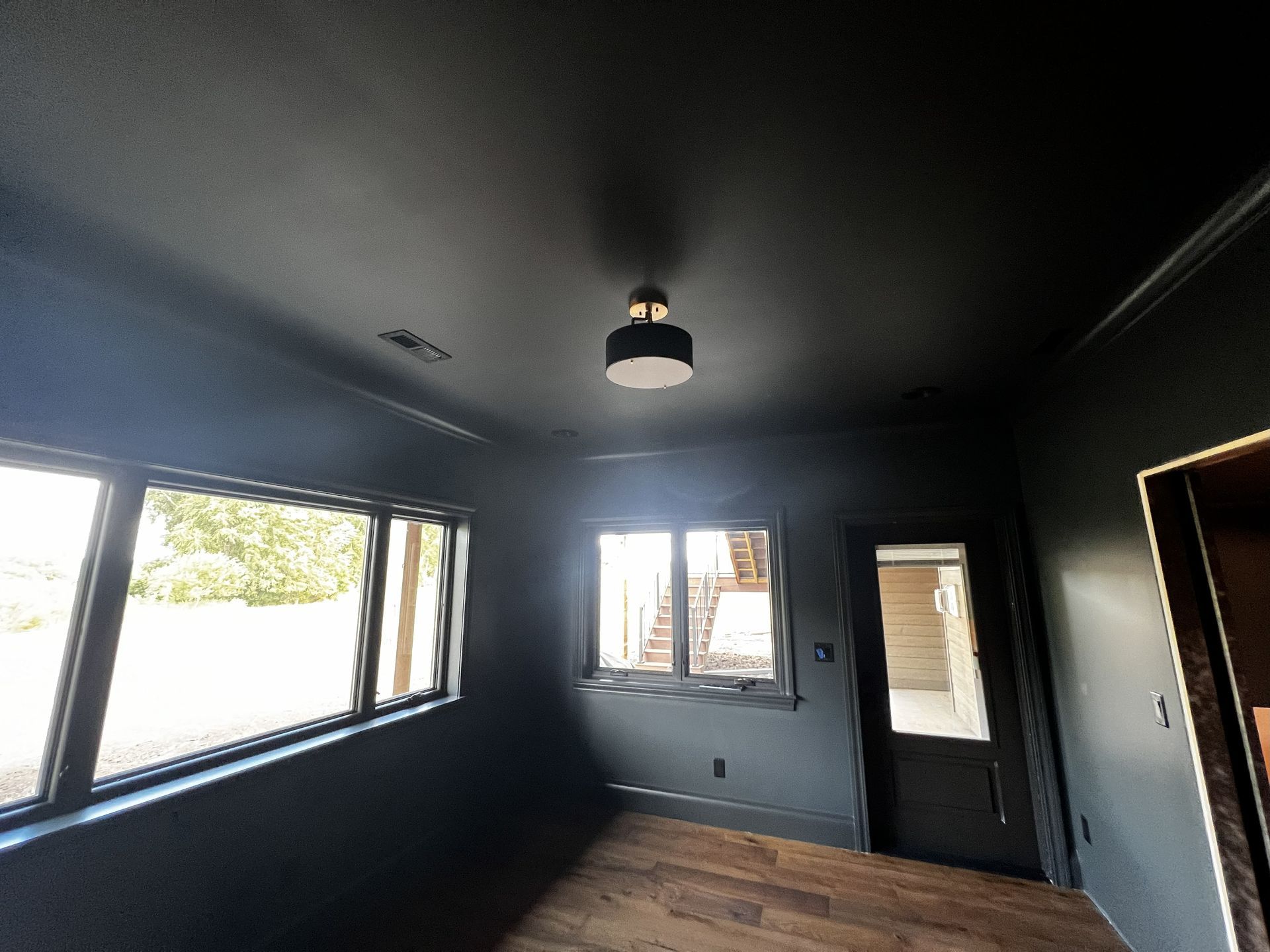 Black room with windows and black ceiling; a light fixture hangs in the center. Wooden floor.