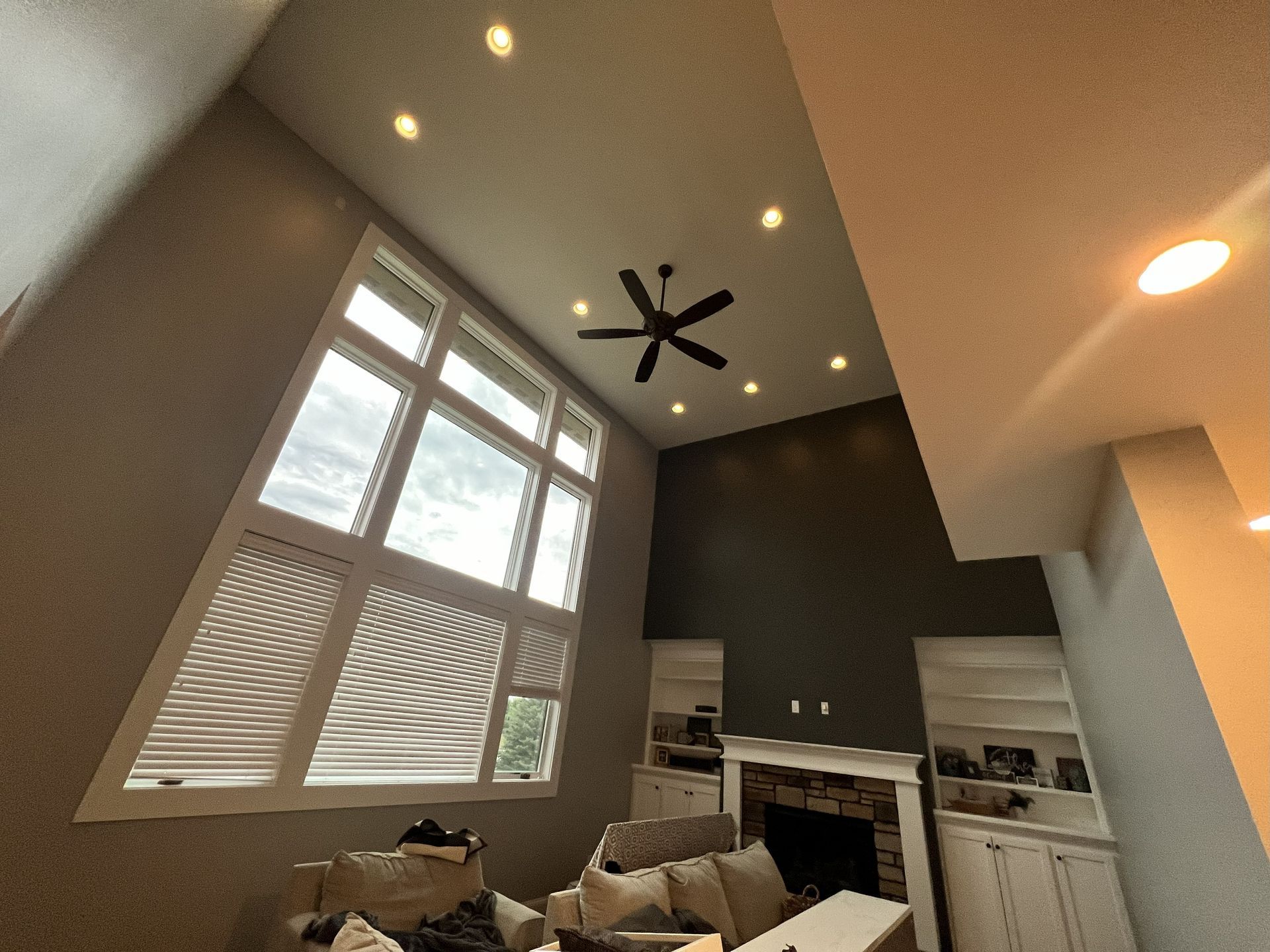Living room with tall windows, dark ceiling fan, recessed lighting, fireplace, and gray walls.