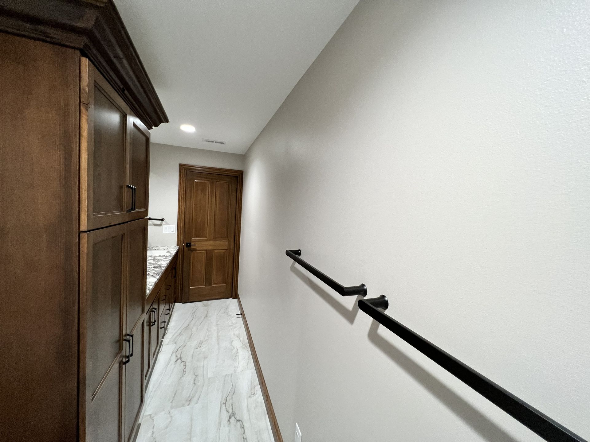 Hallway with dark cabinets, light-colored walls, black handrail, and wooden door.