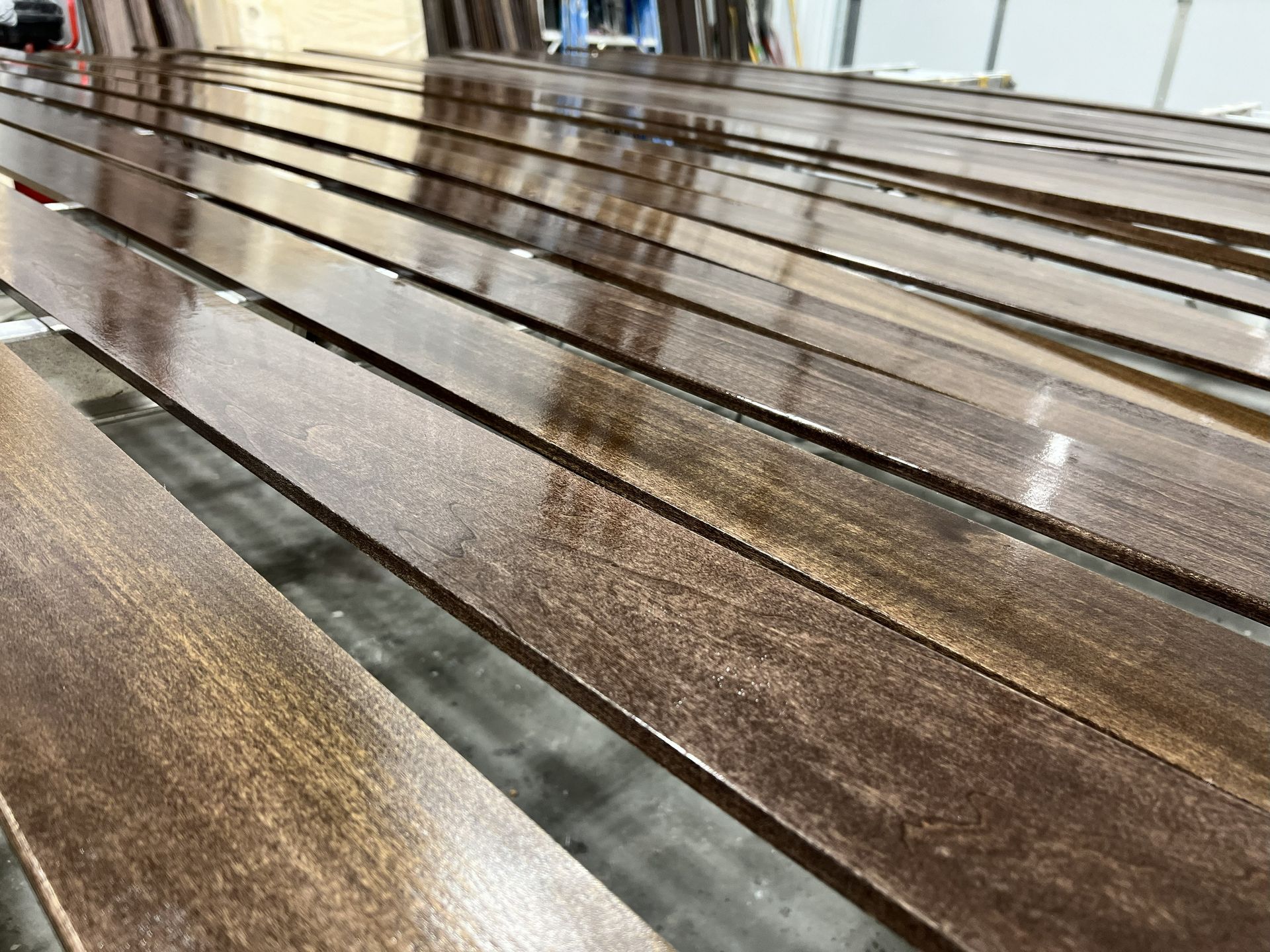 Long, stained wood planks, wet with a glossy finish, arranged in rows on a rack.