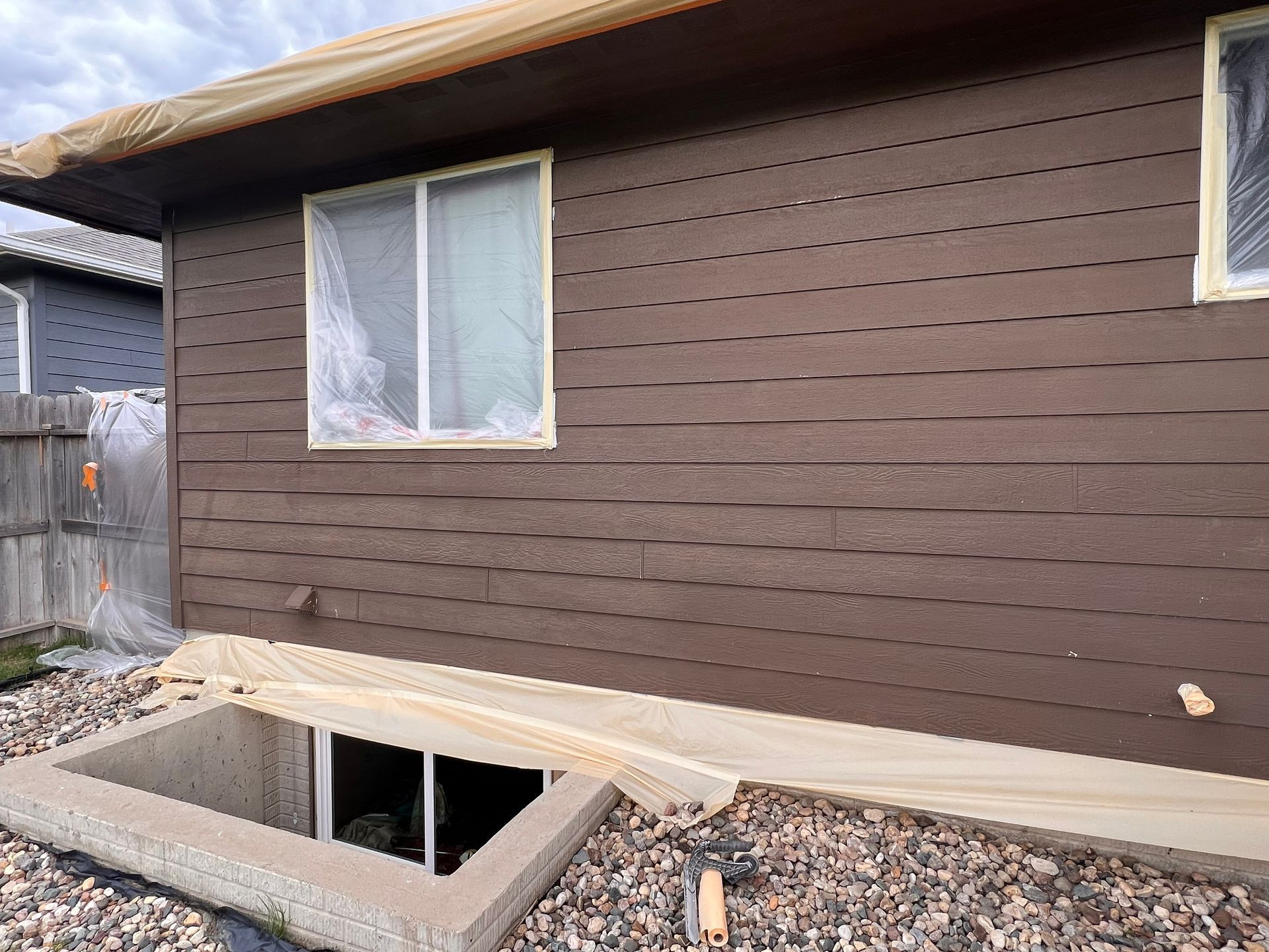 Brown house exterior being painted, windows and foundation covered with plastic.