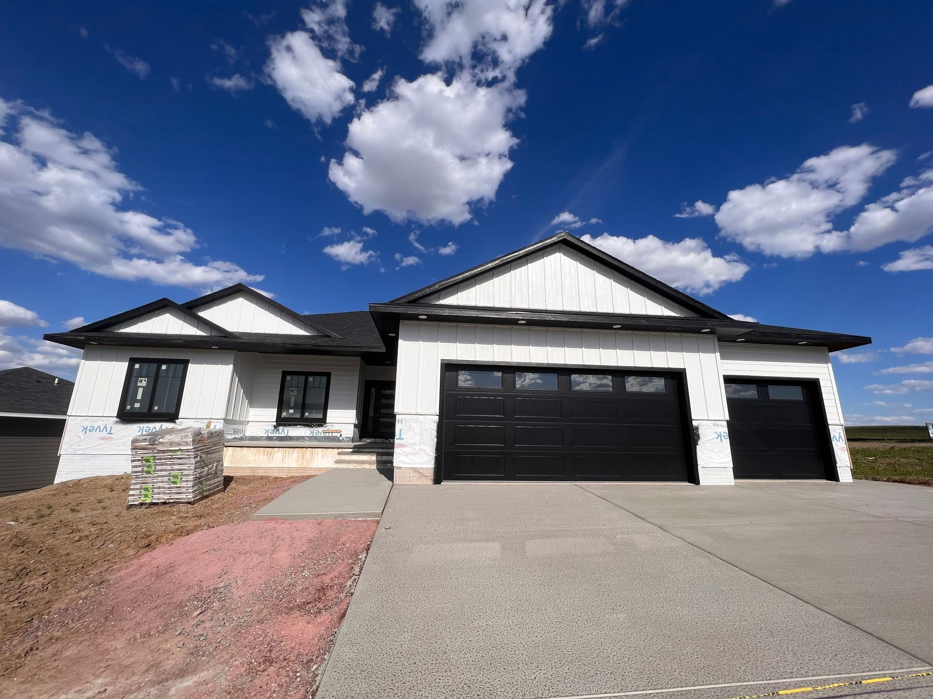 Newly constructed white house with black garage doors and trim, blue sky background.