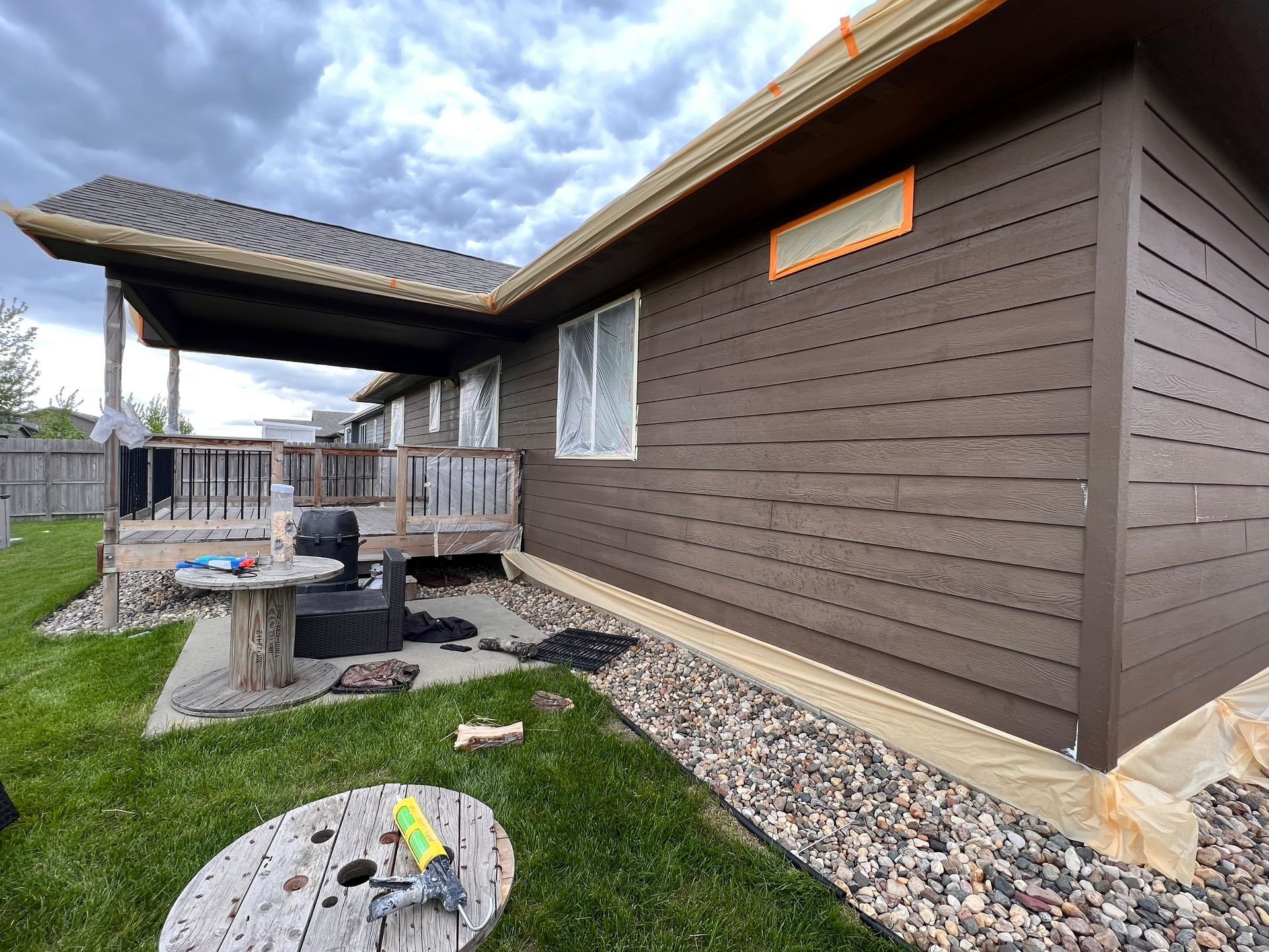 Brown siding on a house with a deck and backyard. Overcast day.