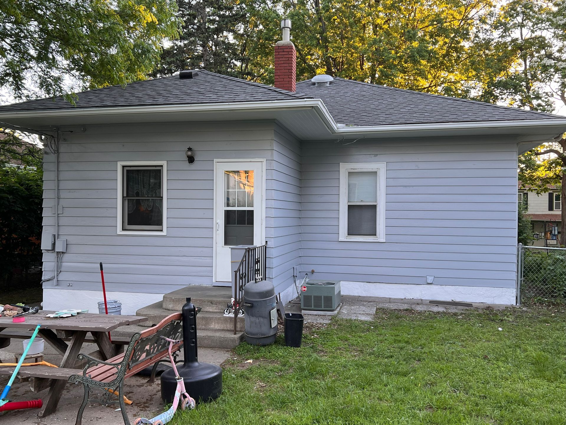 A gray house with a red chimney, white door and windows, and a grassy backyard.